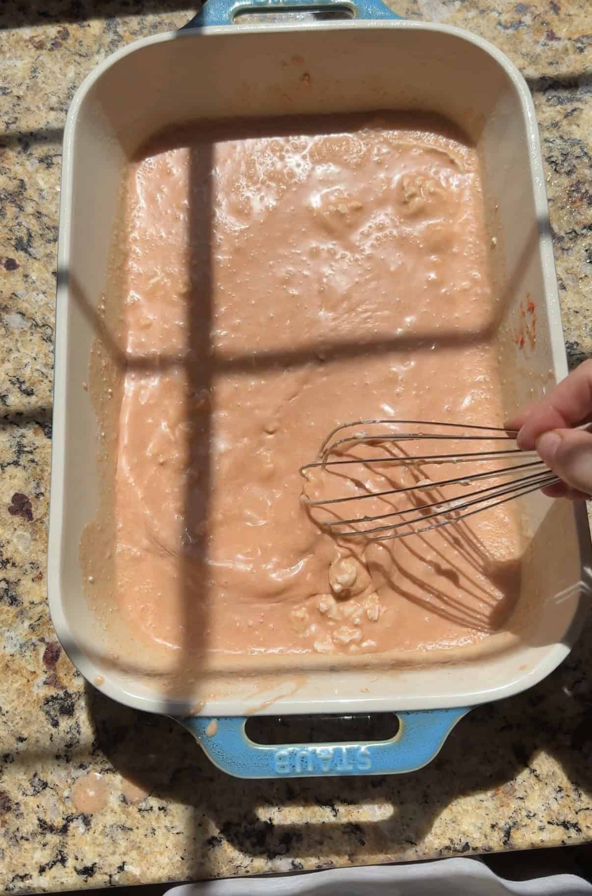 whisking coconut milk, curry, and spices in a blue ceramic 9x13 dish.