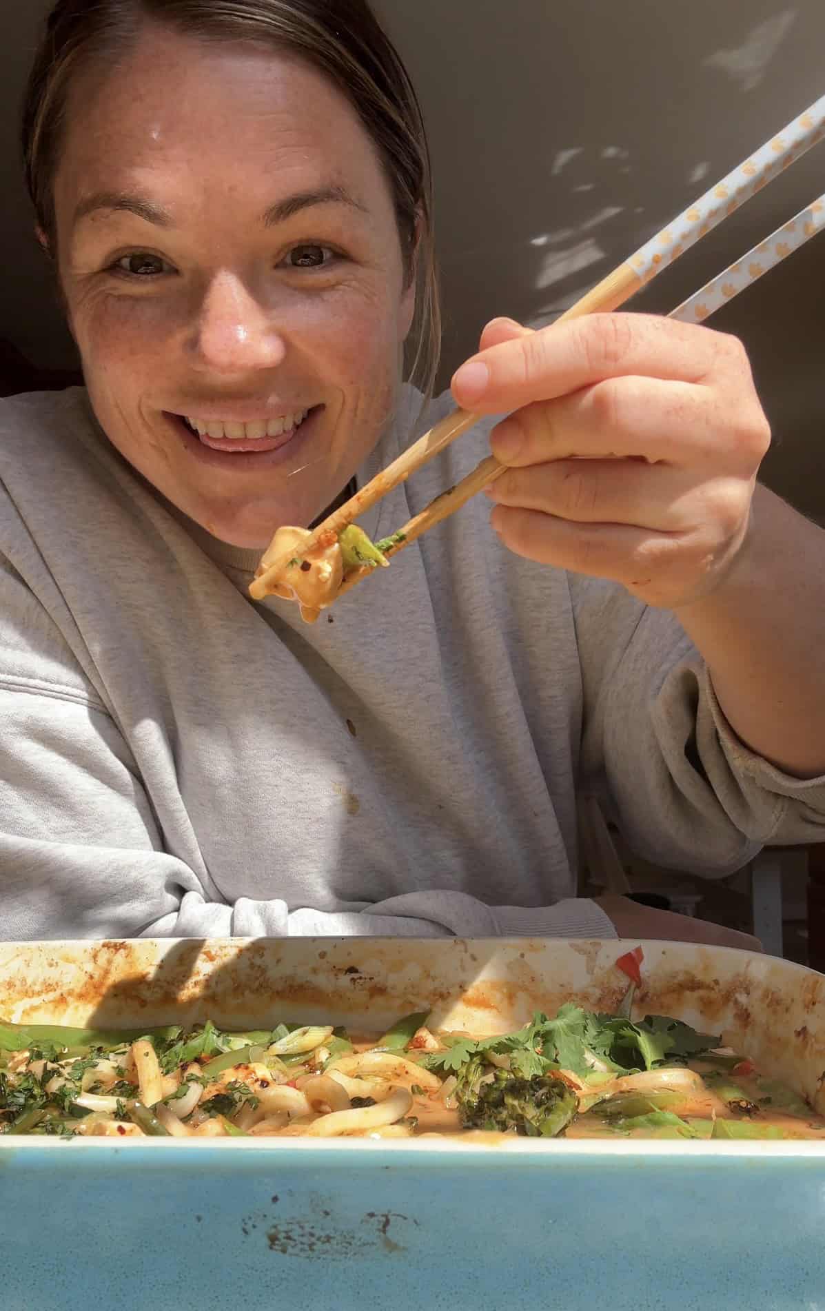 molly holding a bite of coconut chicken curry with chopsticks.