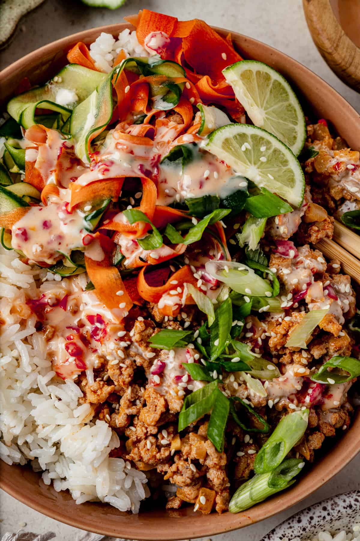 a close up of cucumber carrot salad on top of a ground turkey bang bang bowl.