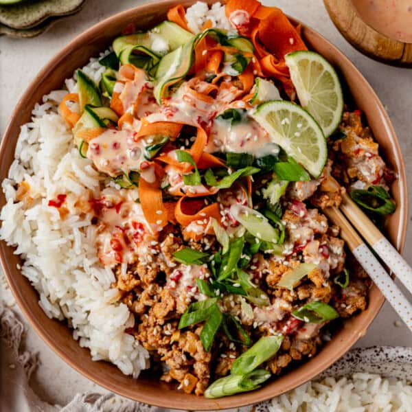 bang bang turkey rice bowl with cucumber carrot salad and chopsticks on the side.