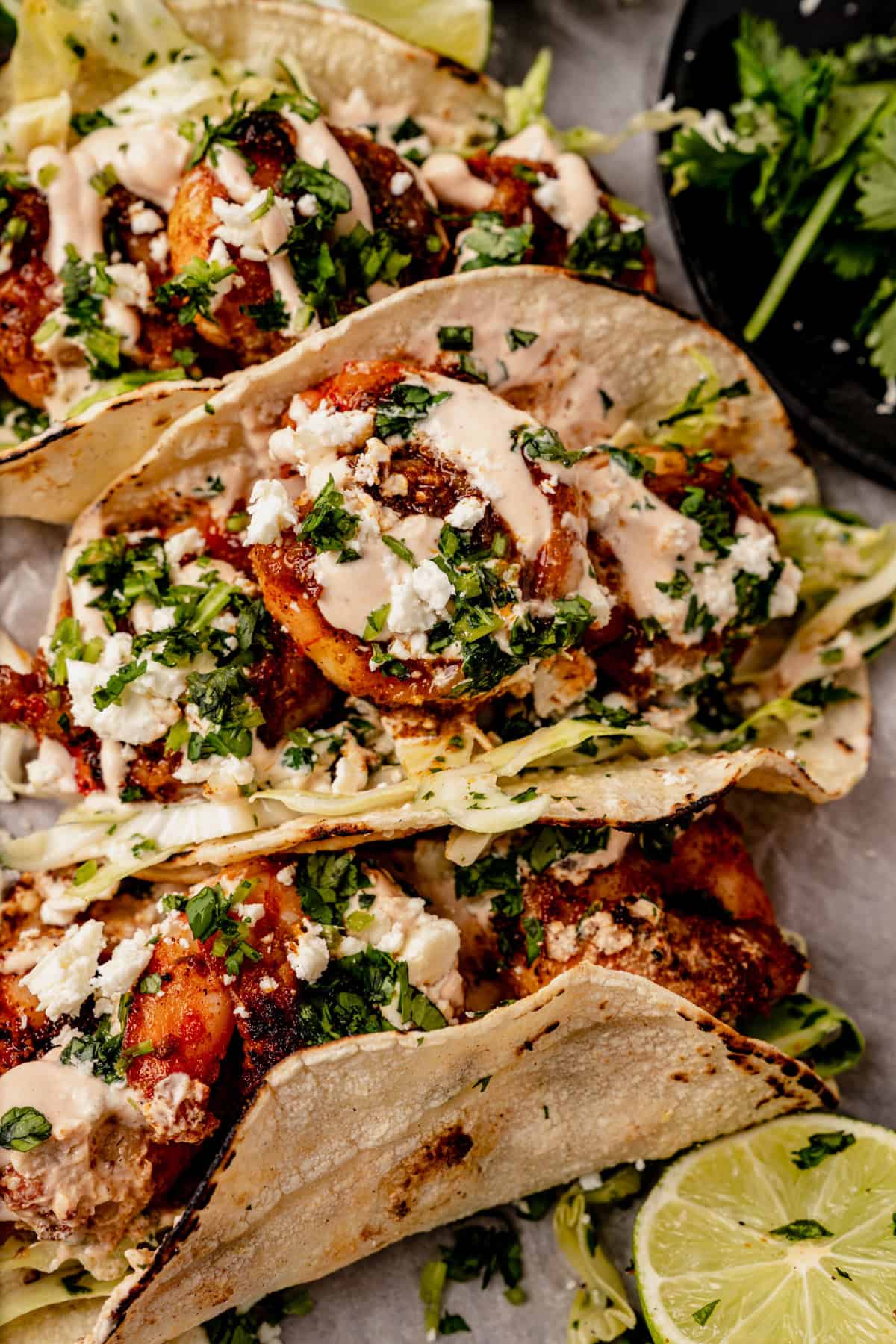 three blackened shrimp tacos on a serving tray with fresh cilantro and a lime wedge.