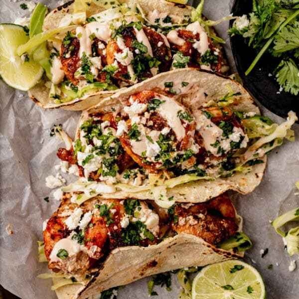 three blackened shrimp tacos on parchment paper topped with chipotle crema and cilantro.