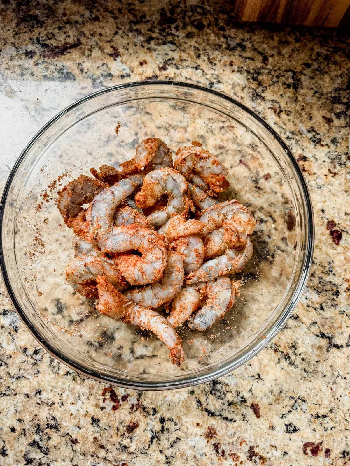 uncooked large shrimp tossed with blackening seasoning in a glass bowl.