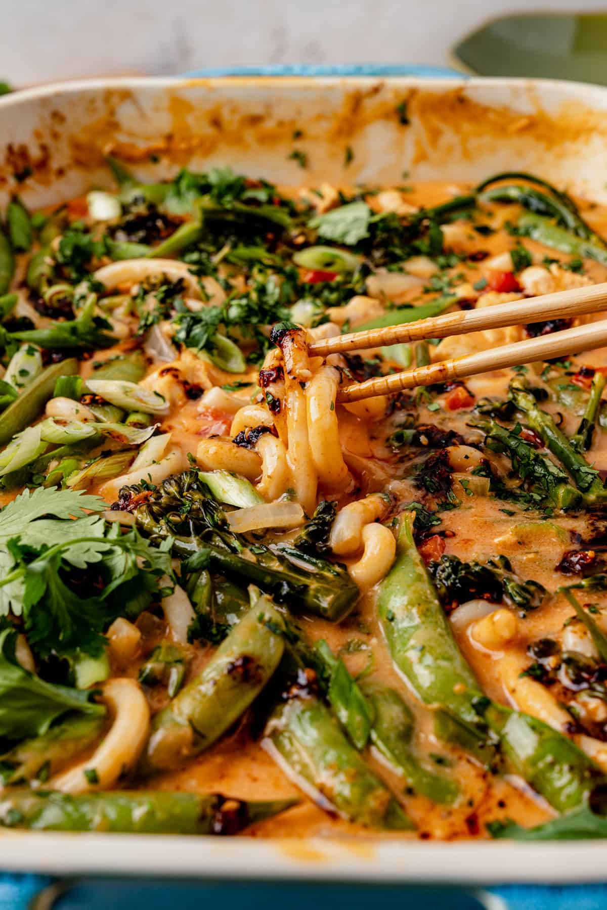 picking up a bite of saucy curry noodles with chicken and vegetables using chopsticks.