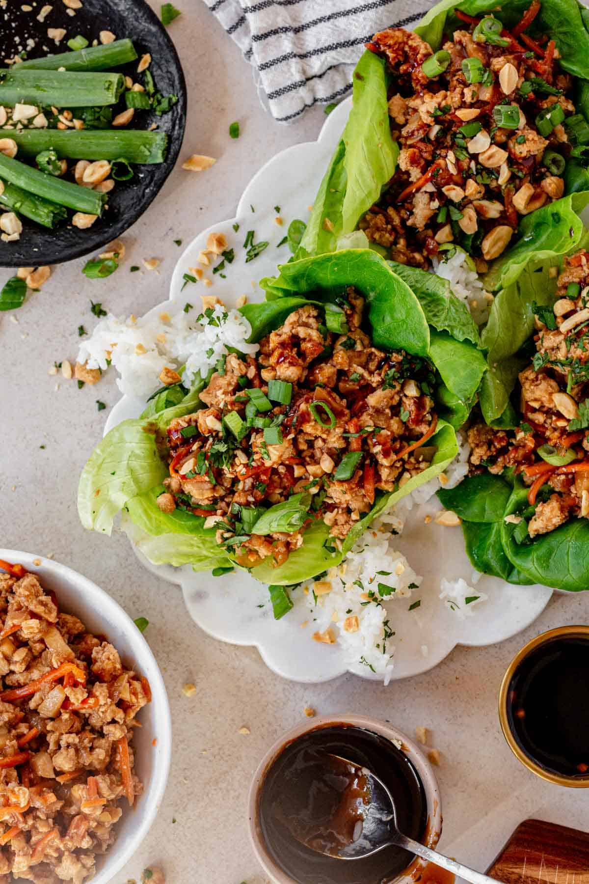 three saucy ground chicken lettuce wraps on a platter topped with cilantro, green onion, and peanuts.