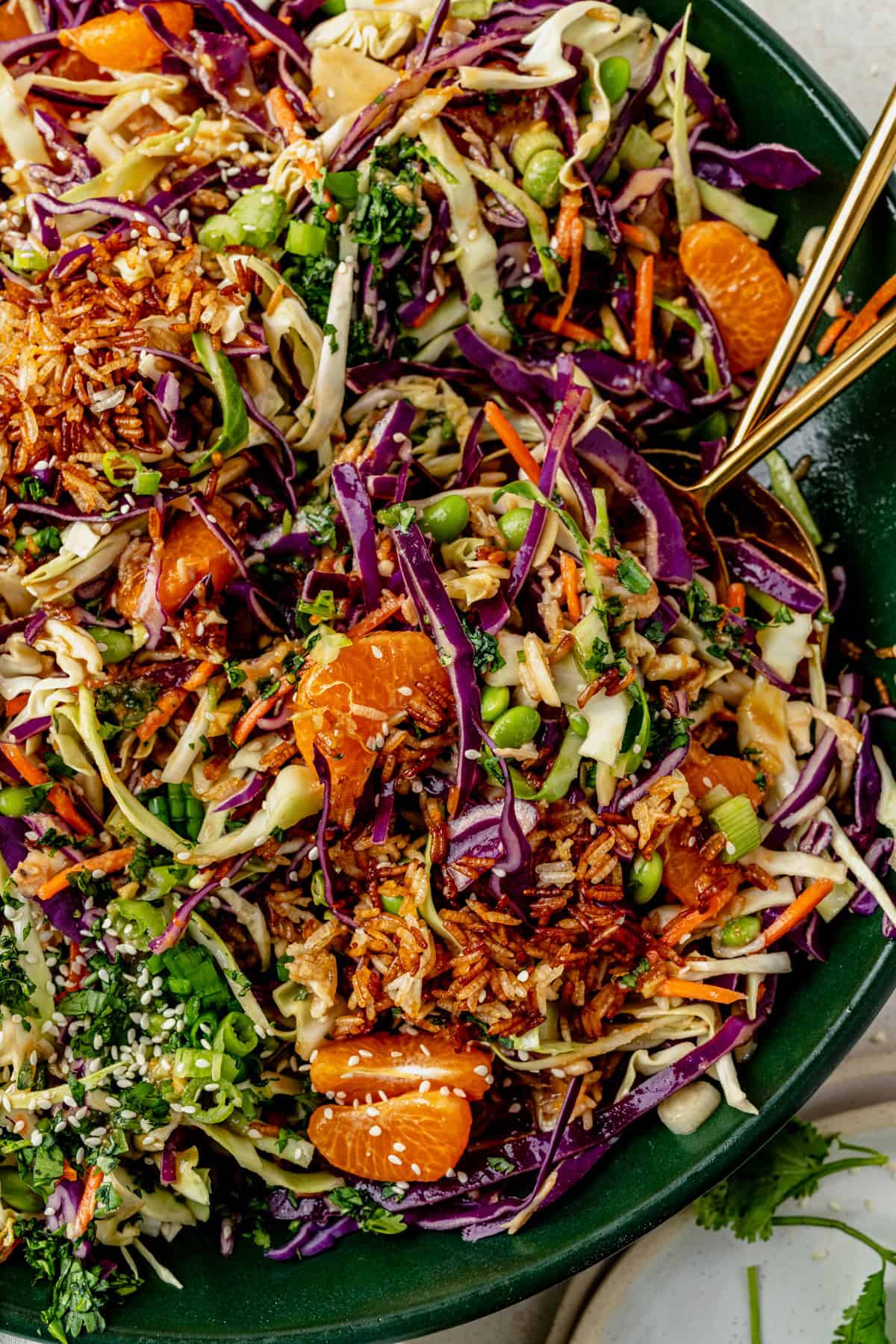 gold serving spoons scooping up mandarin orange chicken salad from a bowl.