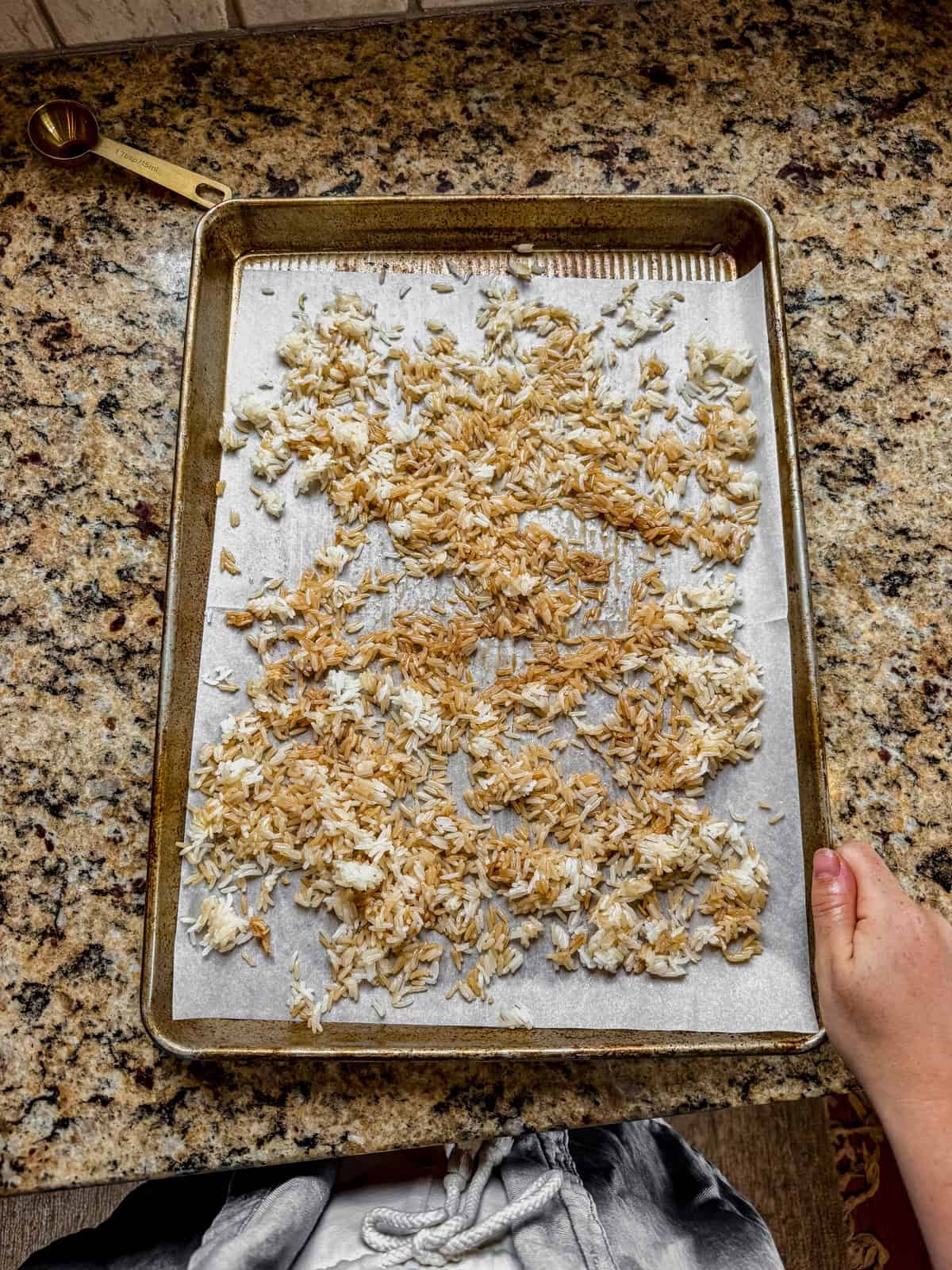 cooked rice tossed in soy sauce and sesame oil spread out on a sheet pan before baking.