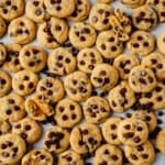 a sheet pan full of mini chocolate chip cookies with a few broken in half to see the soft centers.