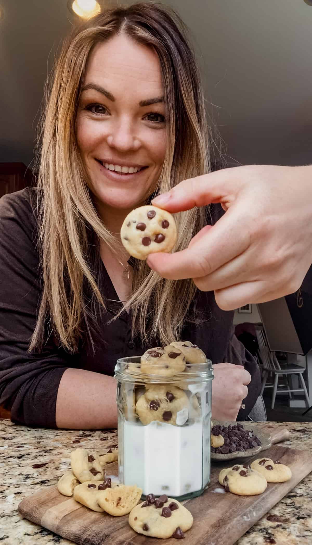 molly thompson holding a mini chocolate chip cookie with a glass of milk next to her.