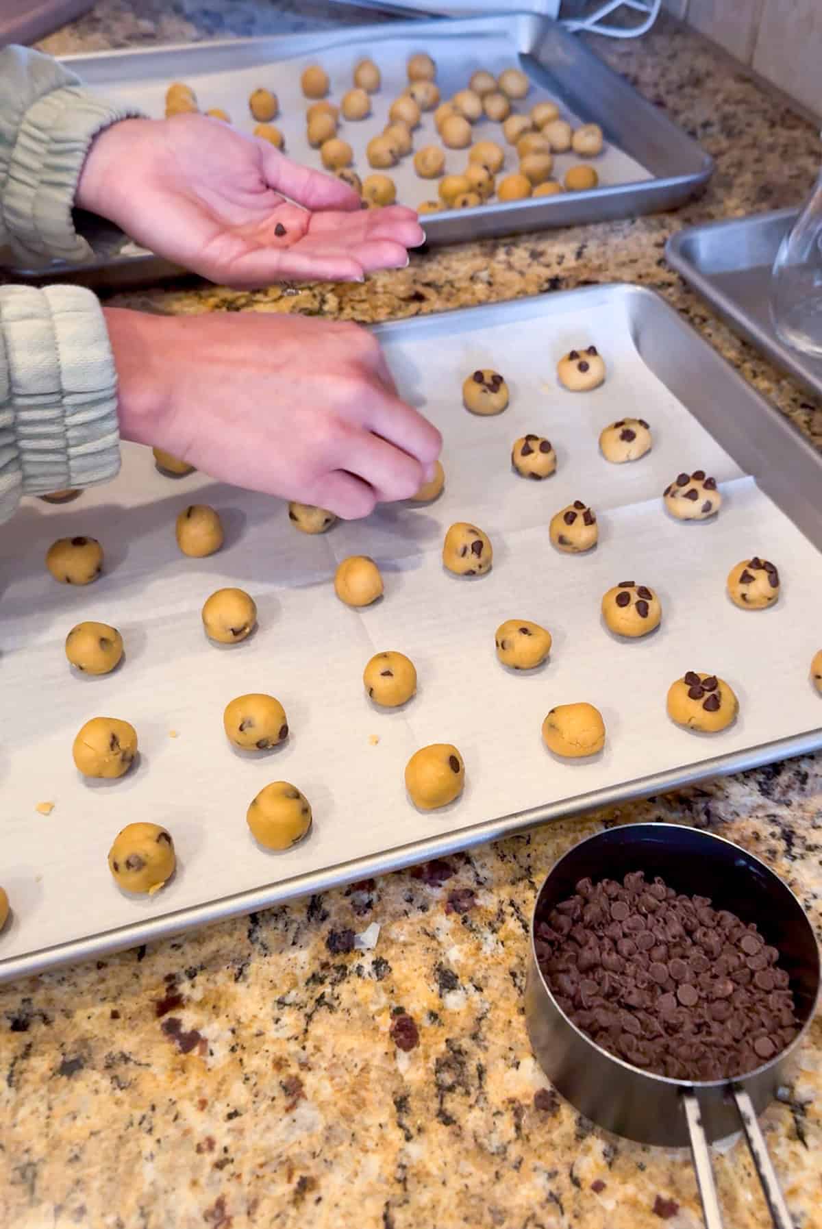 rolling mini chocolate chip cookies on a baking sheet.