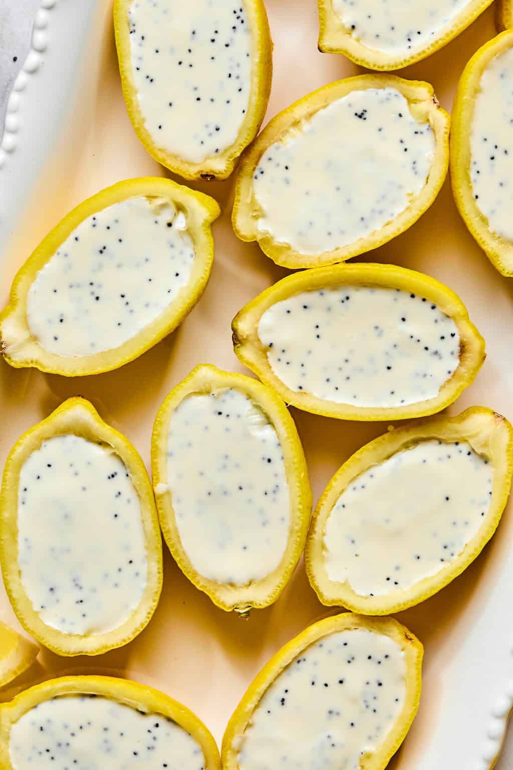 Lemon halves filled with creamy white lemon poppyseed posset are artfully arranged on a white platter.