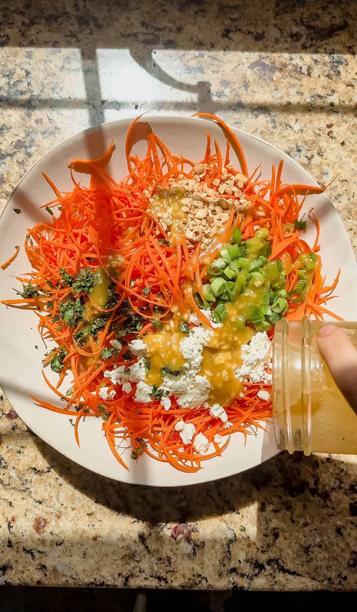 pouring ginger miso salad dressing over shredded carrots, feta, peanuts, green onions, and cilantro.