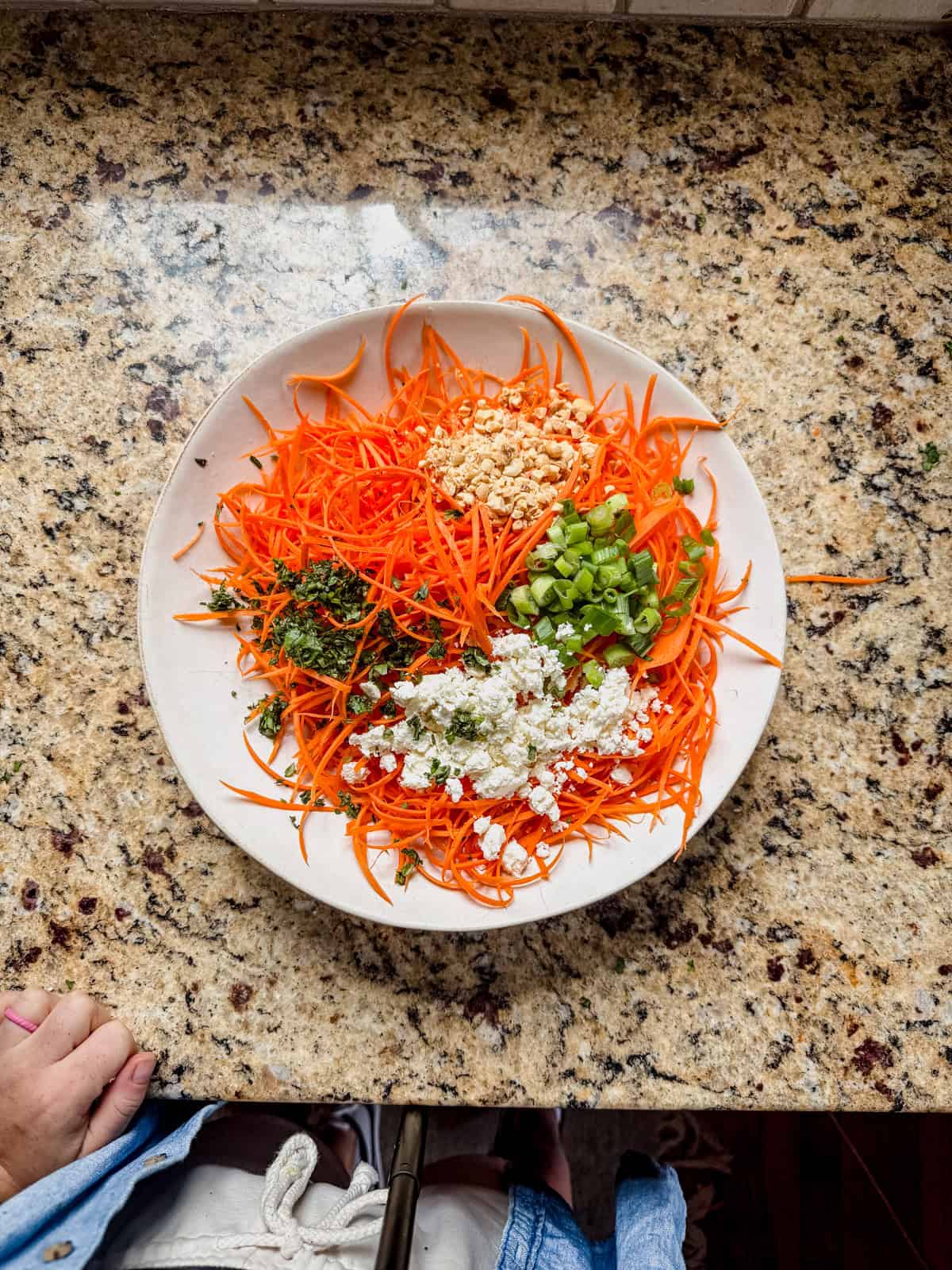 shredded carrots, feta, peanuts, green onions, and cilantro in a white serving bowl on the counter.