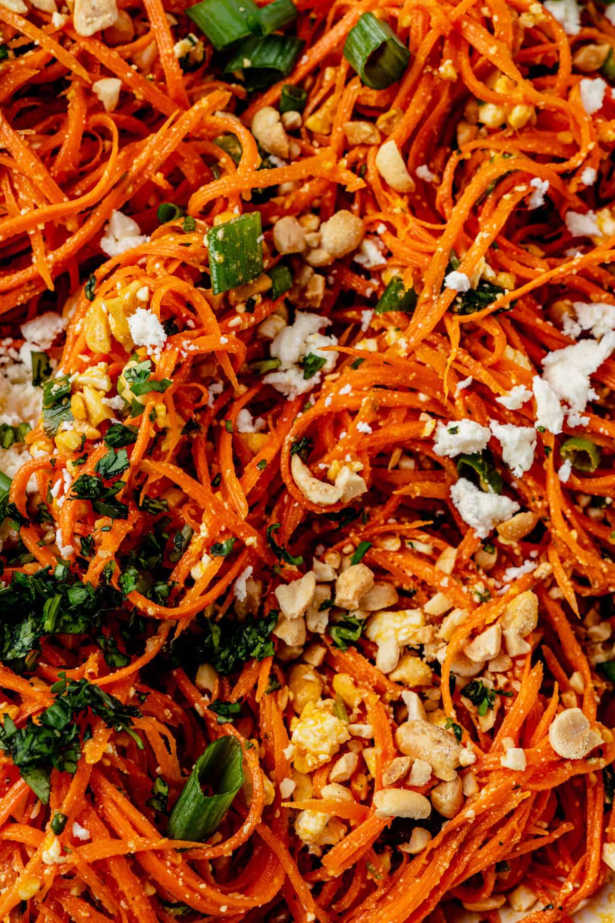 a close up of shredded carrots tossed with feta, peanuts, cilantro, green onion and a ginger dressing.