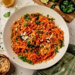 a serving bowl of carrot ginger salad with finely shredded carrots and topped with cilantro and green onions.