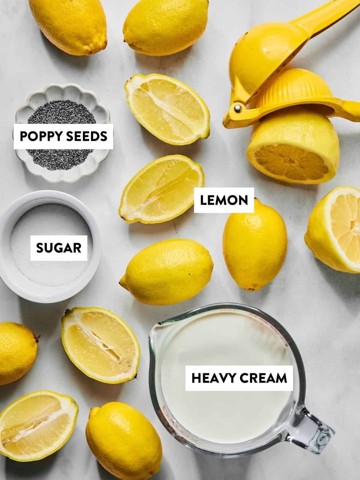 Lemons, lemon halves, a lemon squeezer, a small bowl of poppy seeds, sugar, and heavy cream are arranged on a white surface—each labeled—ready for making a refreshing lemon poppyseed posset.