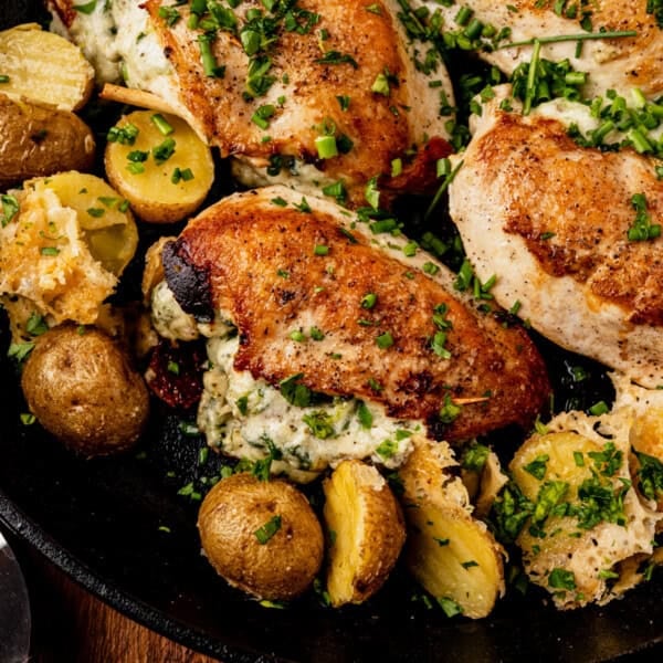 Boursin stuffed chicken breasts with a creamy filling, garnished with chopped herbs, served alongside roasted baby potatoes in a skillet. The dish has a golden-brown, crispy exterior and looks freshly cooked.