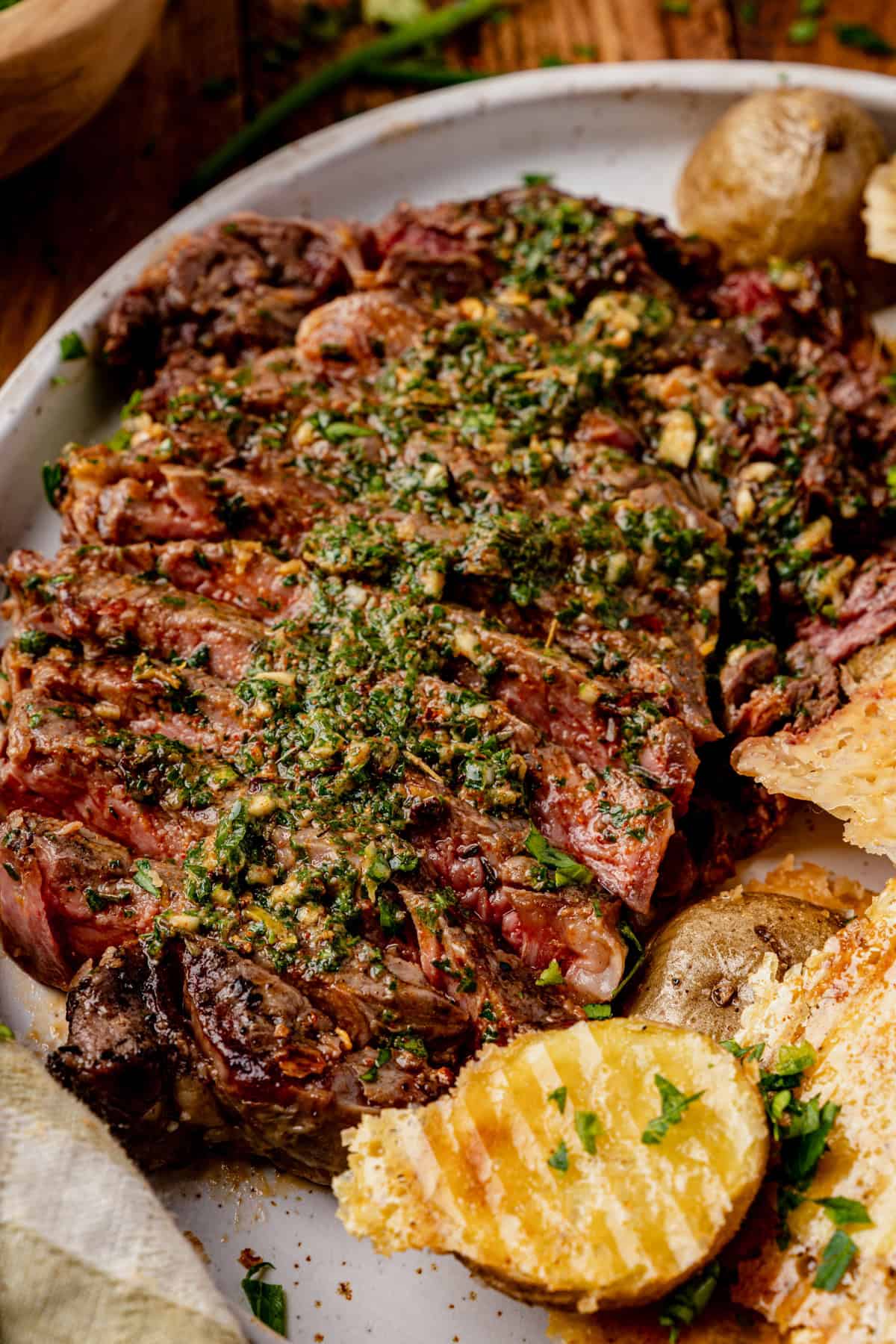 A grilled steak topped with cow butter sauce is served on a plate with roasted potatoes and grilled bread, garnished with fresh herbs.