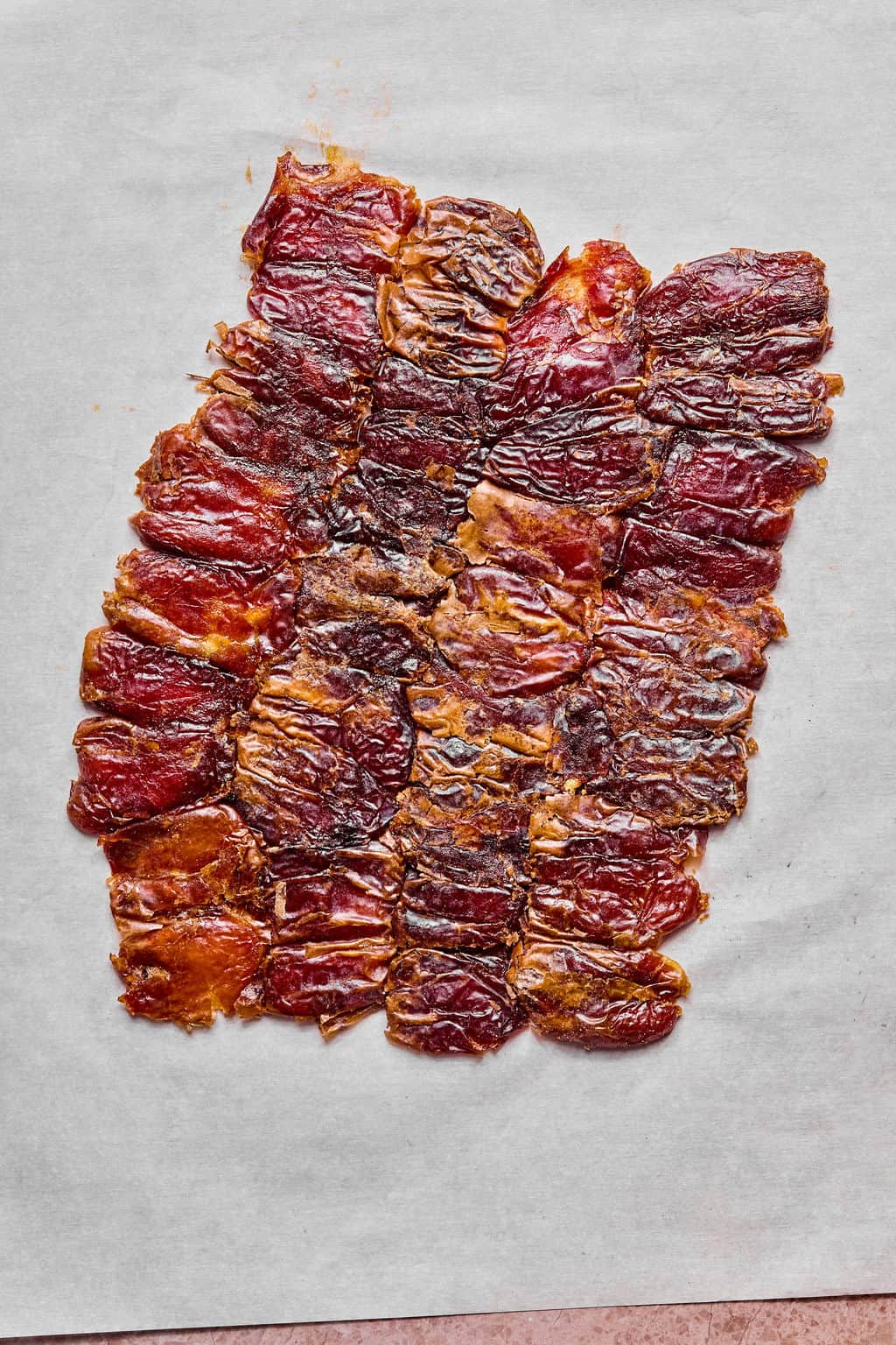 A sheet of thin, overlapping pieces of flattened dates arranged on white parchment paper.