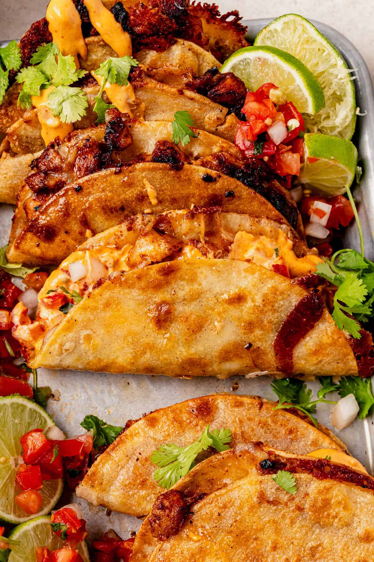 Crispy golden chicken tacos filled with melted cheese and meat, topped with fresh cilantro and served with lime wedges and a side of diced tomato salsa.