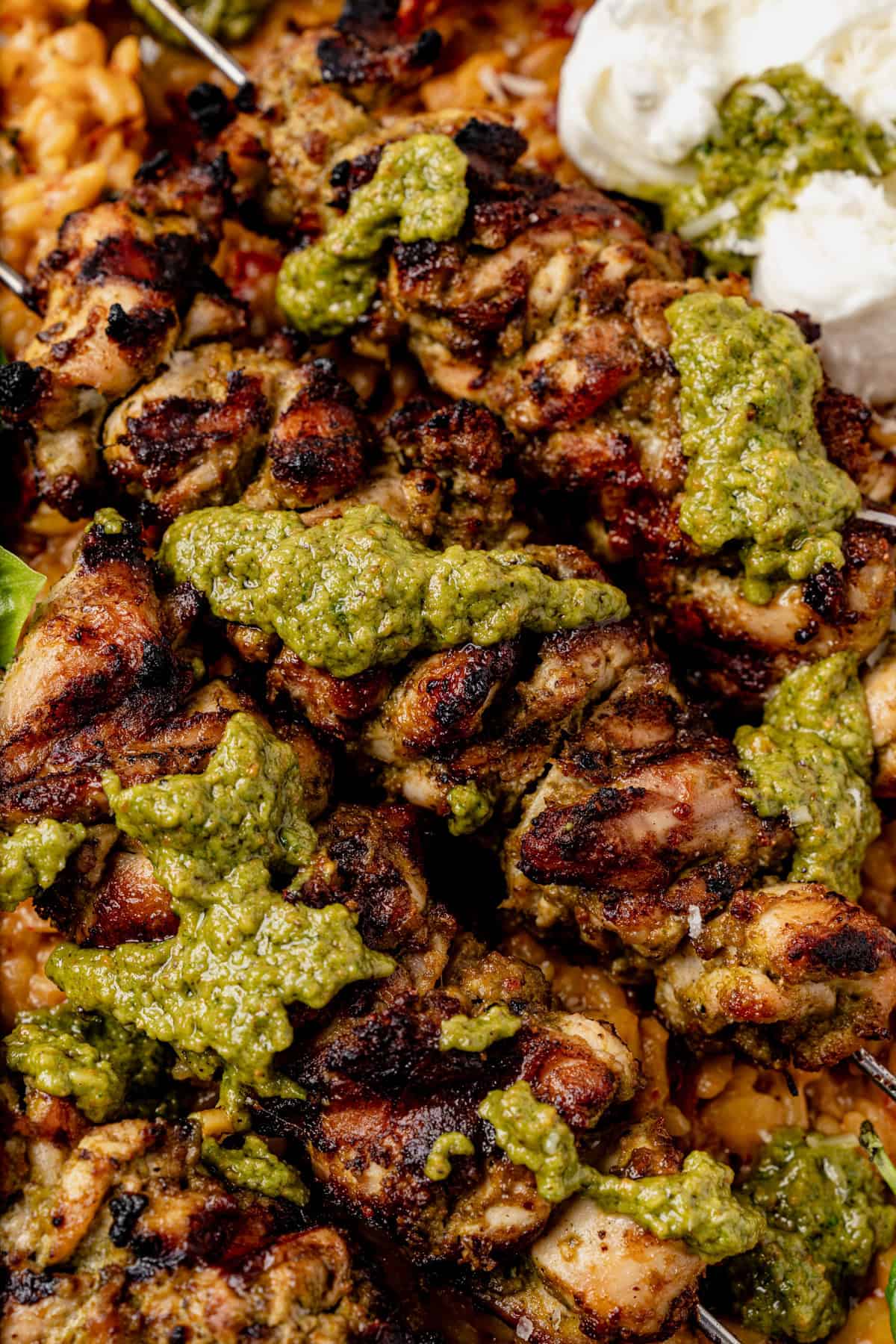Pesto grilled chicken skewers topped with pesto sauce, served over a bed of rice with a dollop of burrata on the side.