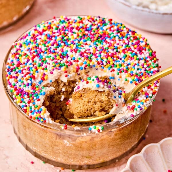A glass bowl of viral protein dot cake topped with colorful nonpereil sprinkles, with a spoon scooping out a bite, showing the fluffy cake inside.