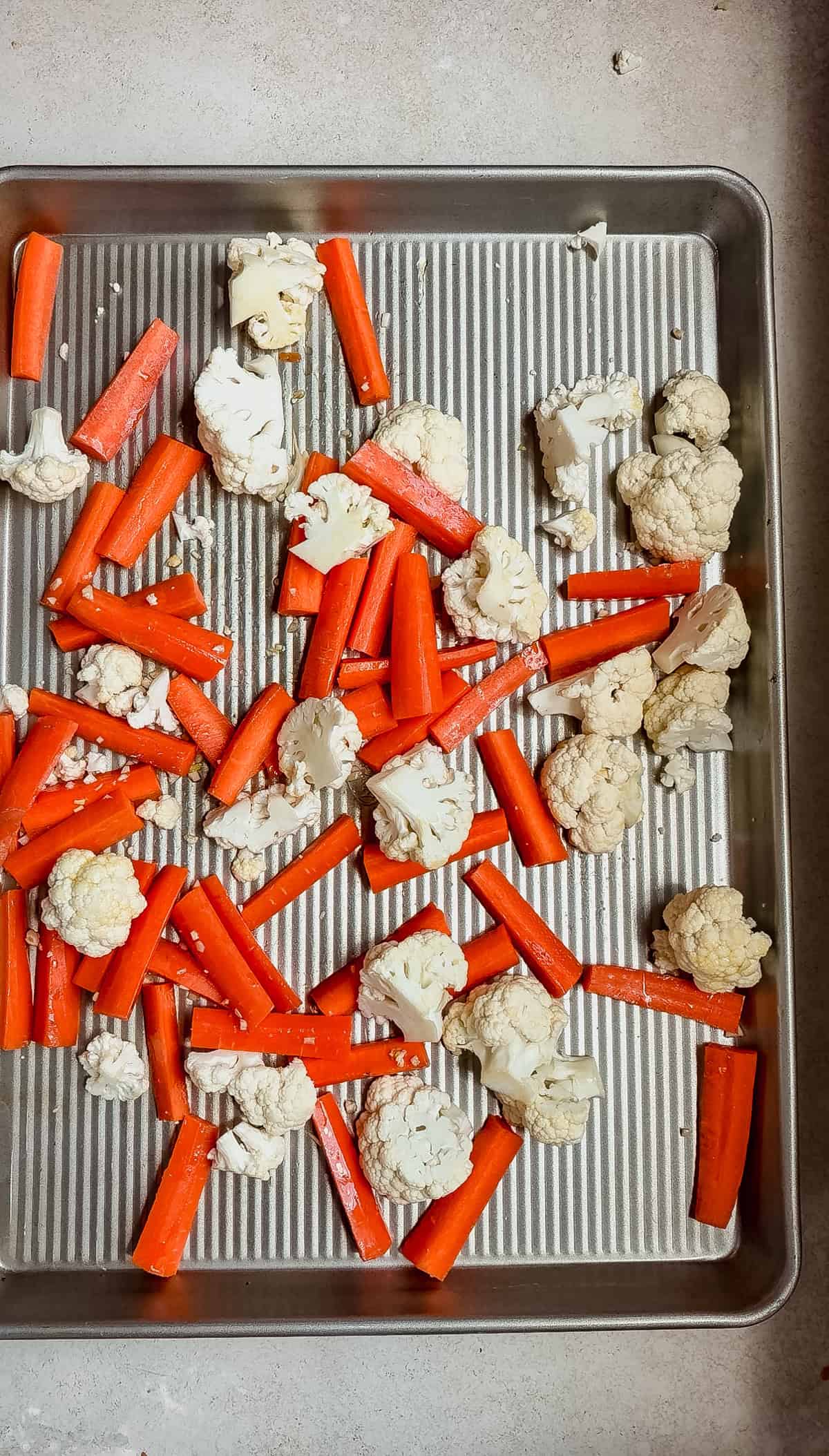 A metal baking sheet with raw cauliflower florets and carrot sticks spread out, ready for roasting alongside flavorful harissa salmon.