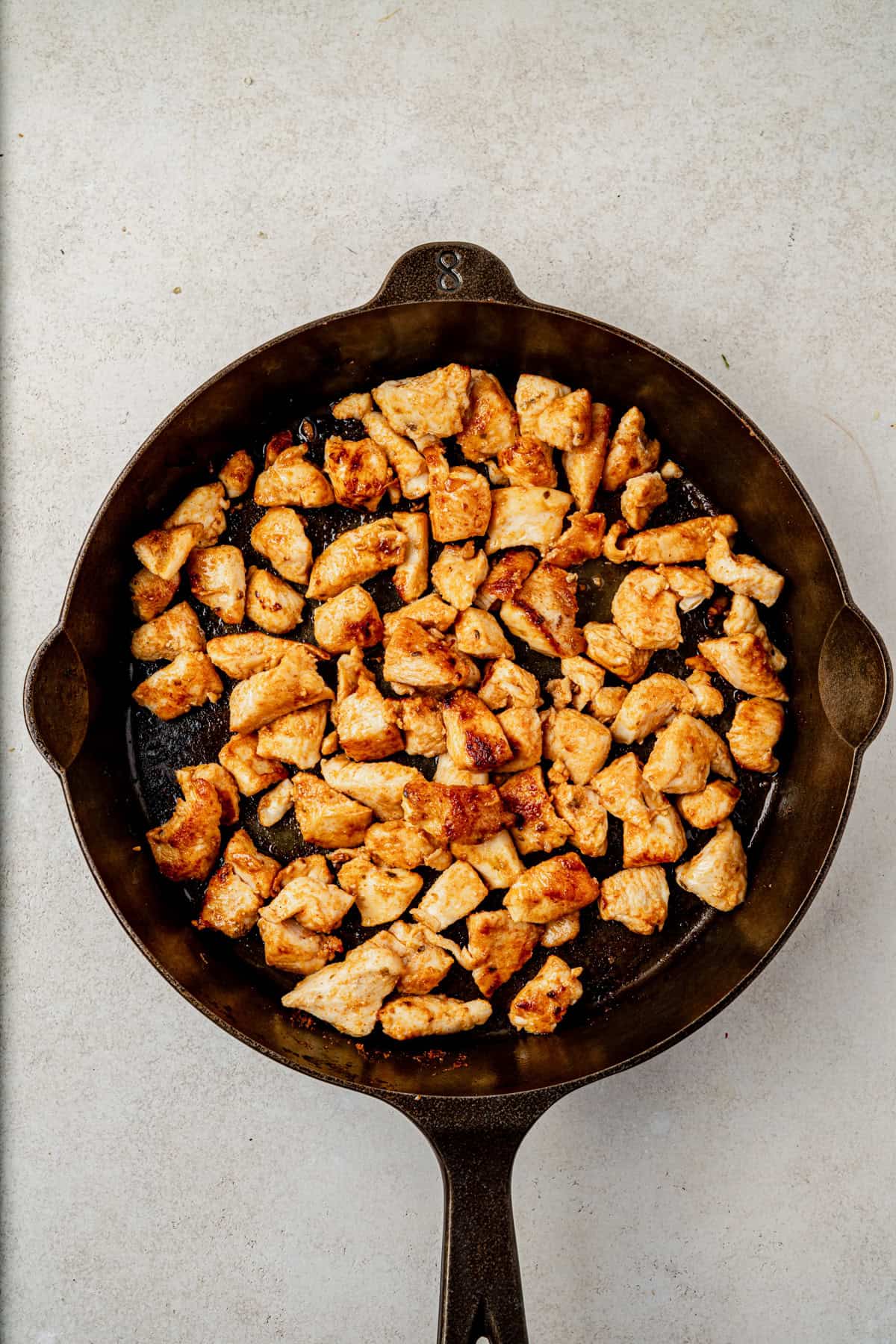 Cooked, seasoned chicken pieces in a cast iron skillet on a light-colored countertop, viewed from above.