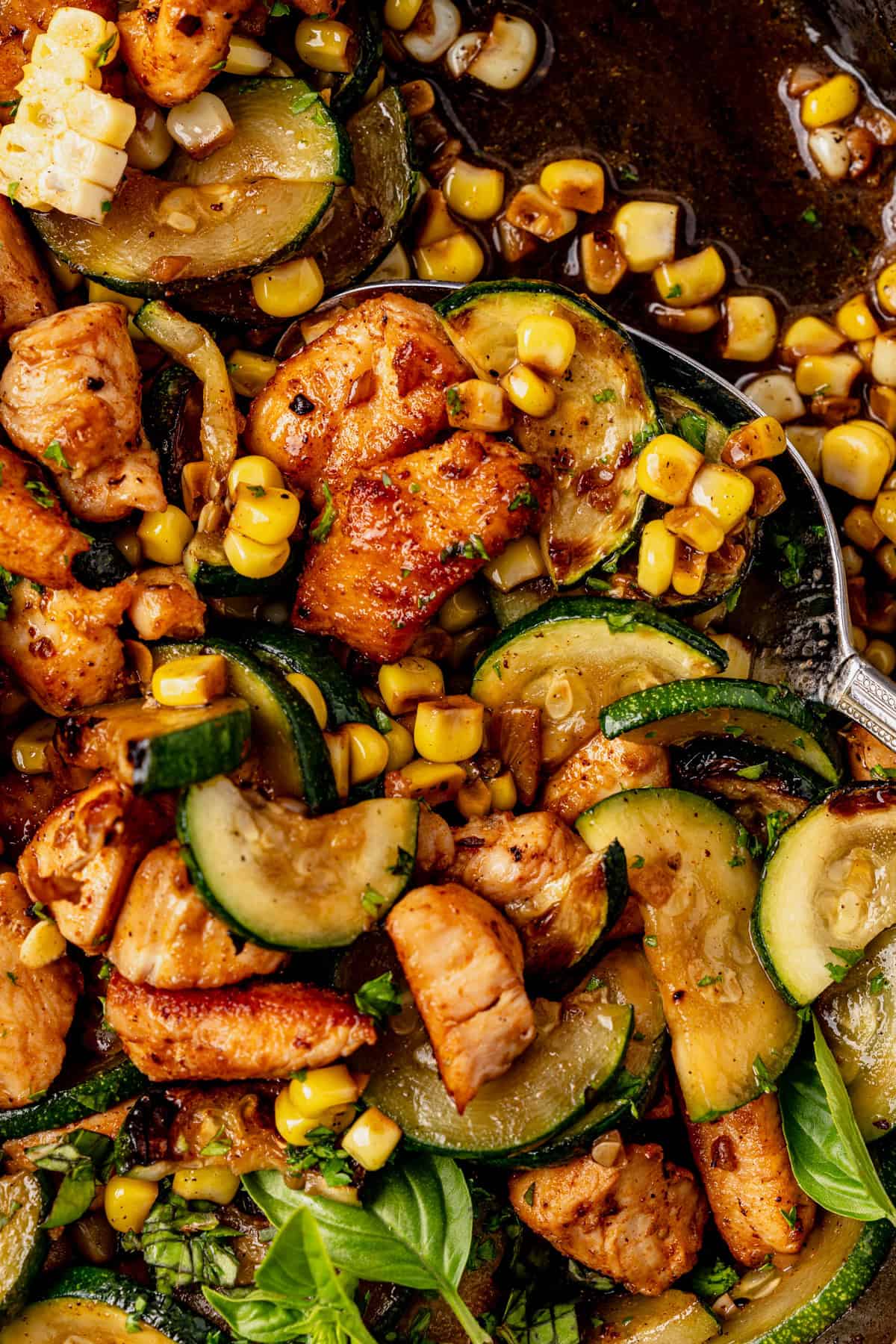Close-up of a chicken zucchini skillet featuring sautéed chicken pieces with zucchini slices, corn kernels, and fresh herbs in a skillet, all glistening with a savory sauce.