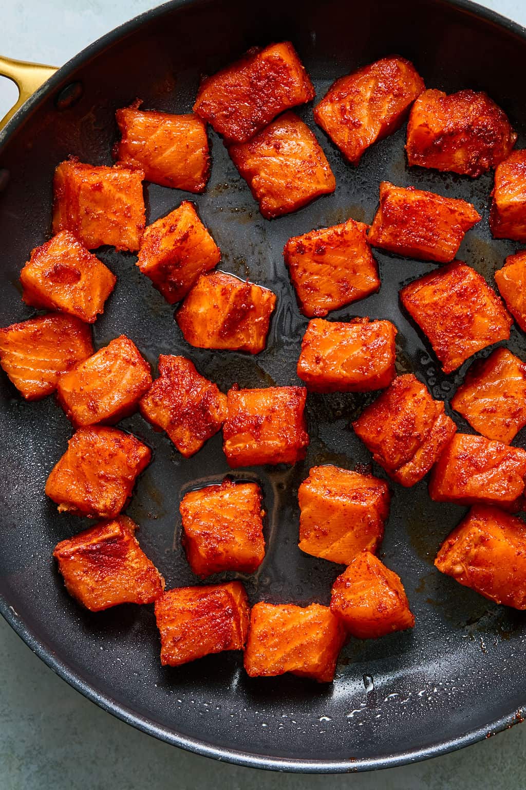 Cubed, seasoned salmon pieces are sizzling in a black frying pan—perfect for building mouthwatering salmon taco bowls. The fish is golden brown and slightly crispy, with visible oil and spices on the surface.