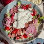 A bowl of blue cheese and steak salad with lettuce, cherry tomatoes, sliced red onions, steak pieces, crumbled cheese, and a large dollop of creamy blue cheese dressing on top.