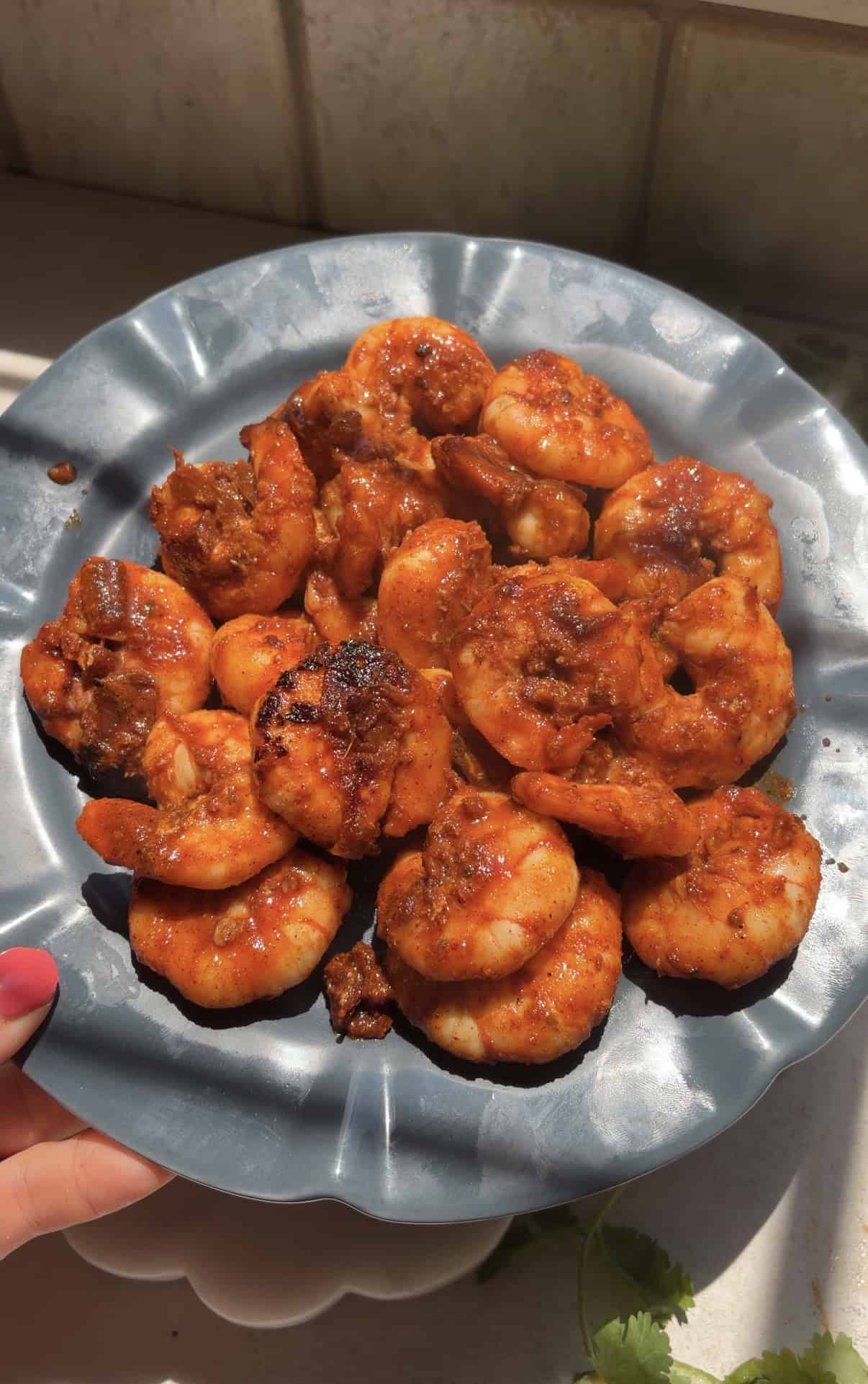 A blue plate holds seared chipotle shrimp, glistening in natural sunlight.