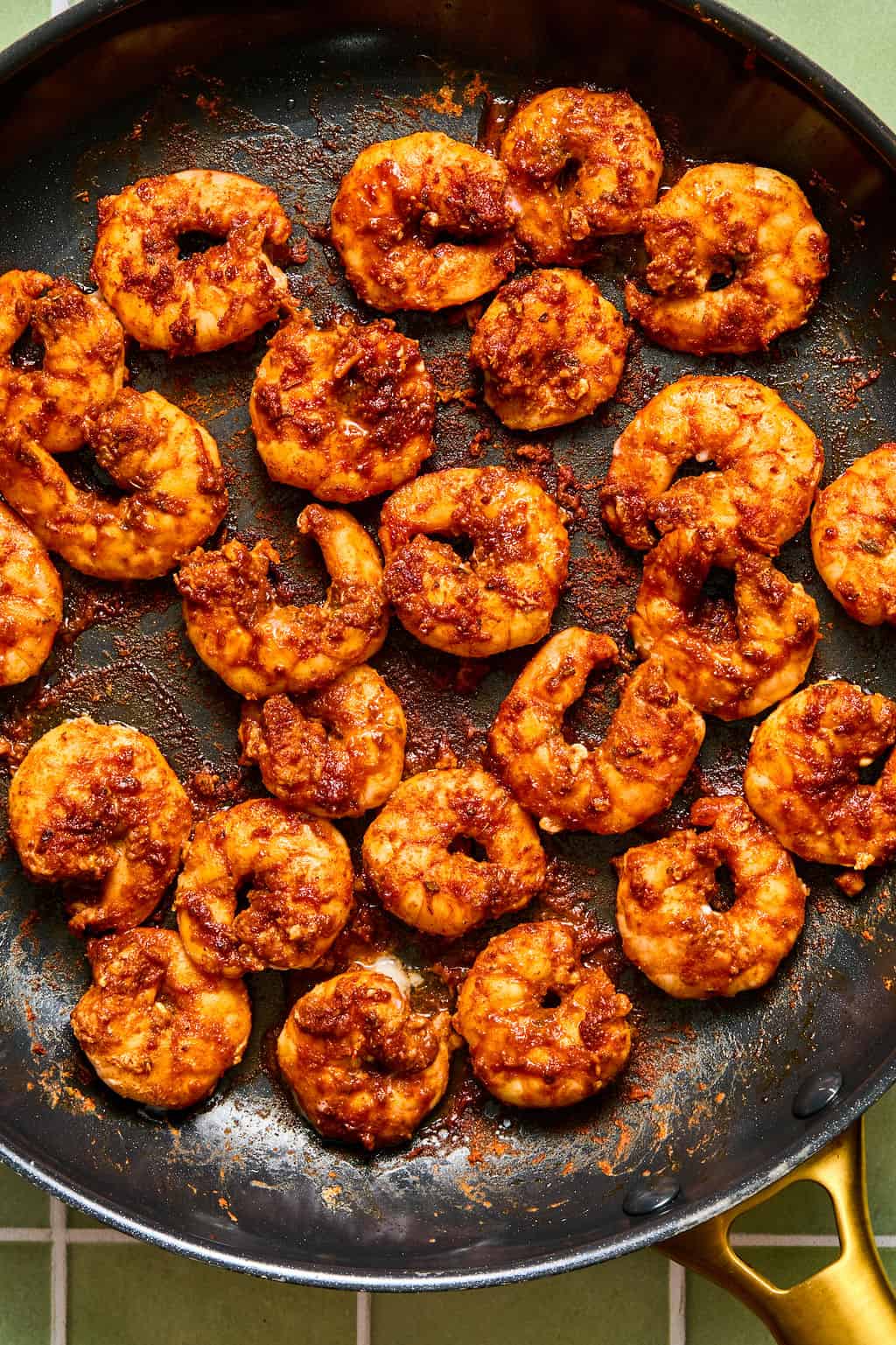 A skillet filled with cooked shrimp coated in a reddish-brown seasoning, reminiscent of the bold flavors in chipotle shrimp tacos, arranged in a single layer on the pan’s surface. The pan handle is visible at the bottom right corner.