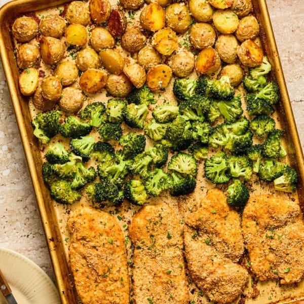 Parmesan crusted chicken sheet pan dinner with crispy golden potatoes, broccoli, and breaded chicken cutlets, all baked and seasoned, on a beige countertop.