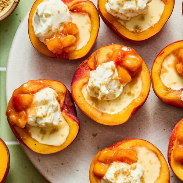 Peach possets topped with whipped cream and a fruit compote, arranged on a white plate. Reminiscent of a peach posset, the peaches are drizzled with syrup and sprinkled with brown sugar.