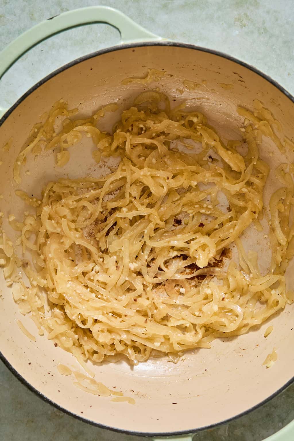 Caramelized onions in a large cream-colored pot, with some browning on the bottom. The onions are soft, golden, and evenly spread across the pots surface.