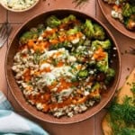 A buffalo chicken bowl filled with ground chicken, roasted broccoli, blue cheese crumbles, herbs, hot sauce, and a dollop of yogurt on a tiled surface.