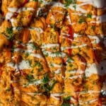 Tray of buffalo chicken stuffed mini bell peppers topped with melted cheese, drizzled with white sauce, and sprinkled with chopped herbs, shown in bright lighting.