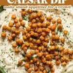 Bowl of creamy Caesar dip topped with roasted chickpeas and herbs, surrounded by pieces of toasted bread. Text overlay reads: Cold Chicken Caesar Dip. Make ahead appetizer for a crowd..