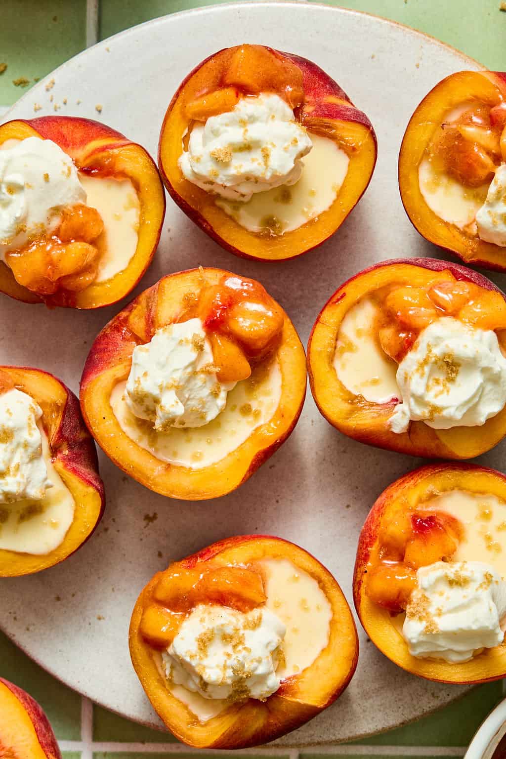 Halved peaches topped with whipped cream, a drizzle of sauce, and sprinkled brown sugar, arranged on a round white plate.