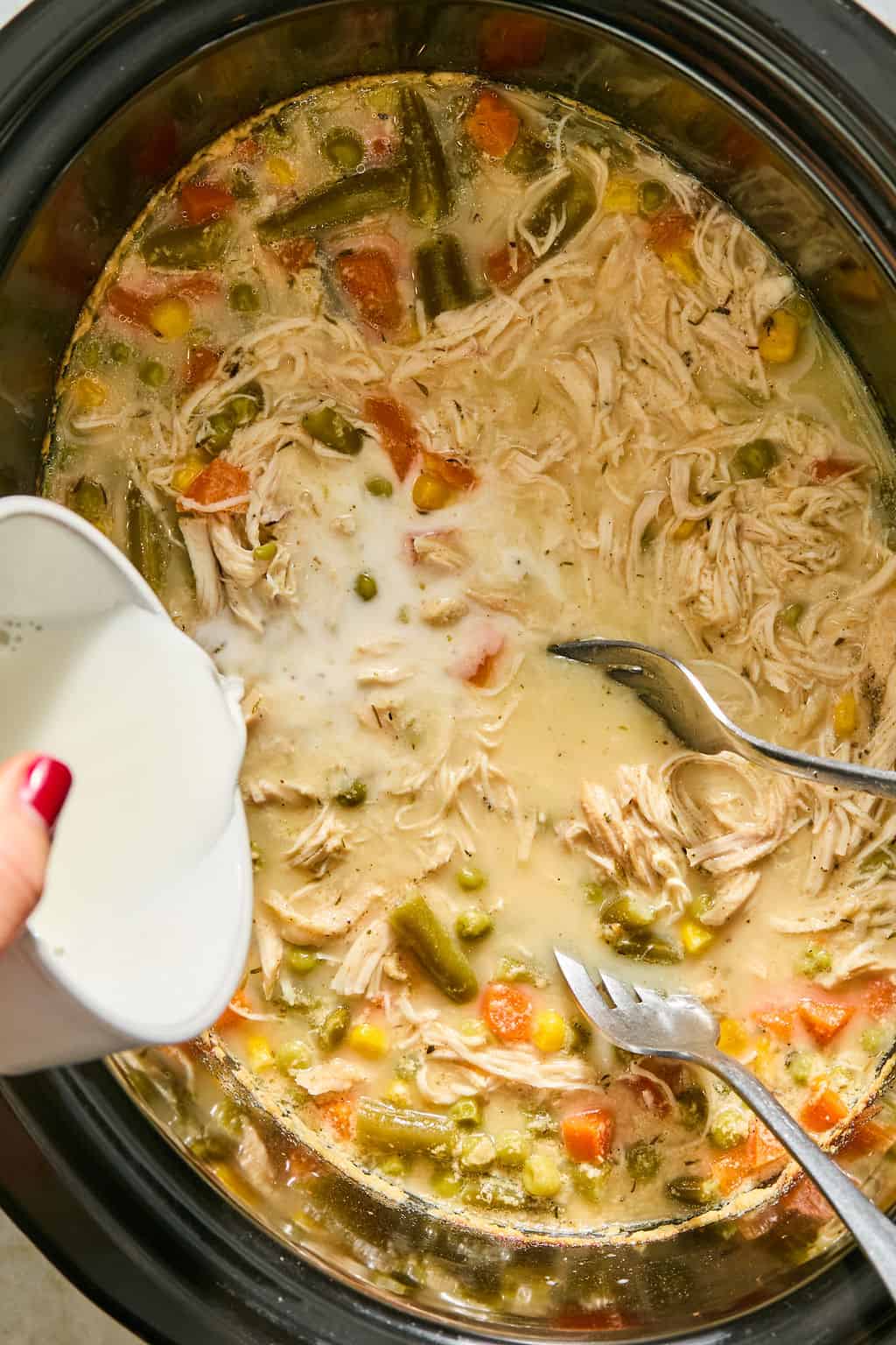 A hand pours cornstarch slurry into slow cooker chicken pot pie.