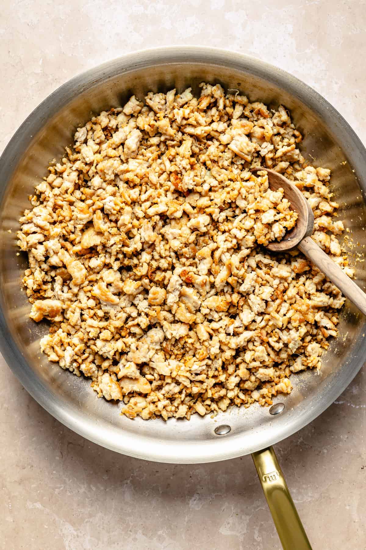 Ground meat browning in a stainless steel skillet with a wooden spoon.
