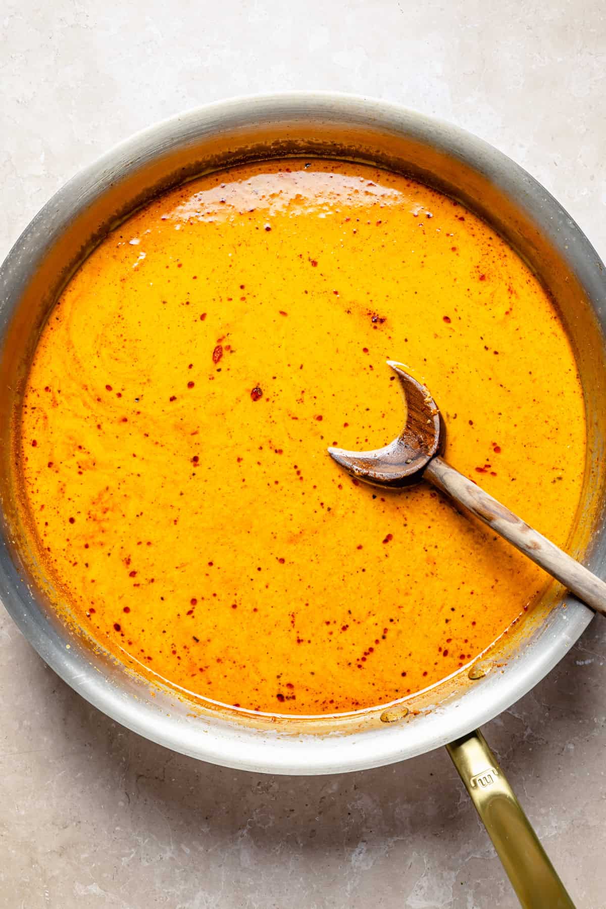 A metal skillet filled with orange curry sauce and a wooden spoon.