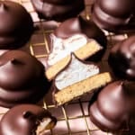 Chocolate-covered marshmallow mallomar cookies on a wire rack, with one cut in half to show a cookie base and marshmallow center.