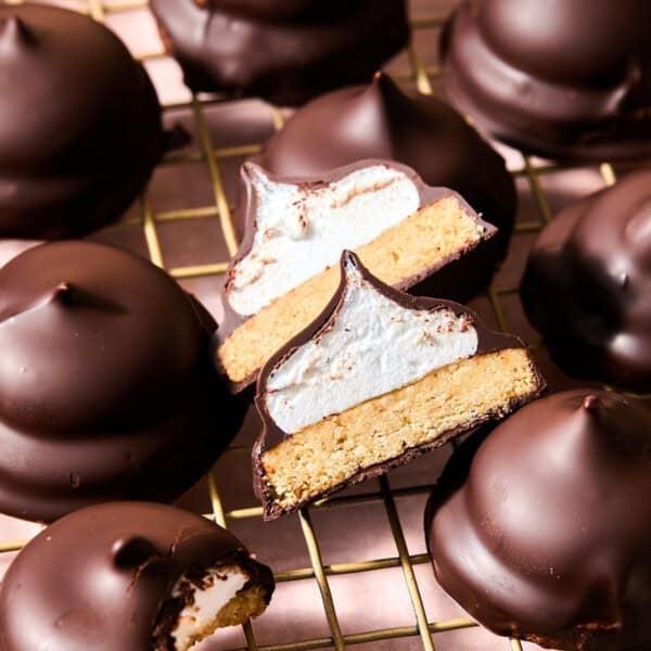 Chocolate-covered marshmallow mallomar cookies on a wire rack, with one cut in half to show a cookie base and marshmallow center.