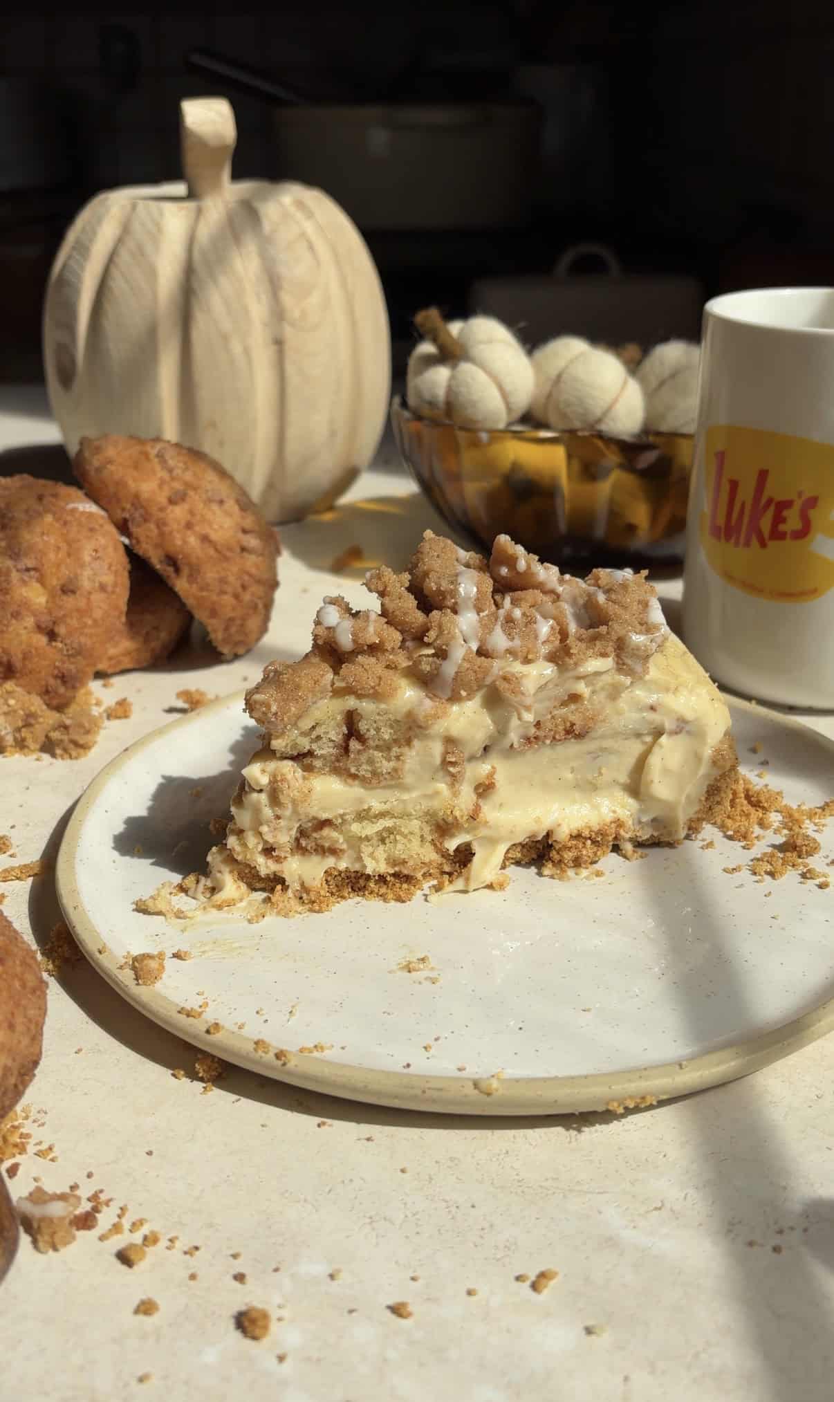 A slice of muffin bottom pie with a creamy filling on a plate, with a coffee mug labeled Lukes and a wooden pumpkin in the background.