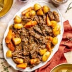 A platter of braised oven pot roast served with potatoes and carrots, garnished with fresh thyme.