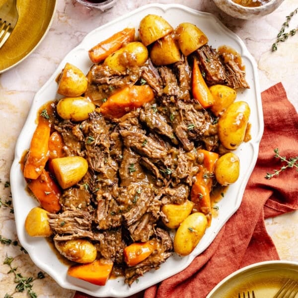 A platter of braised oven pot roast served with potatoes and carrots, garnished with fresh thyme.