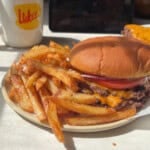 A plate with a cheeseburger and salted french fries, next to a mug with a Lukes logo.