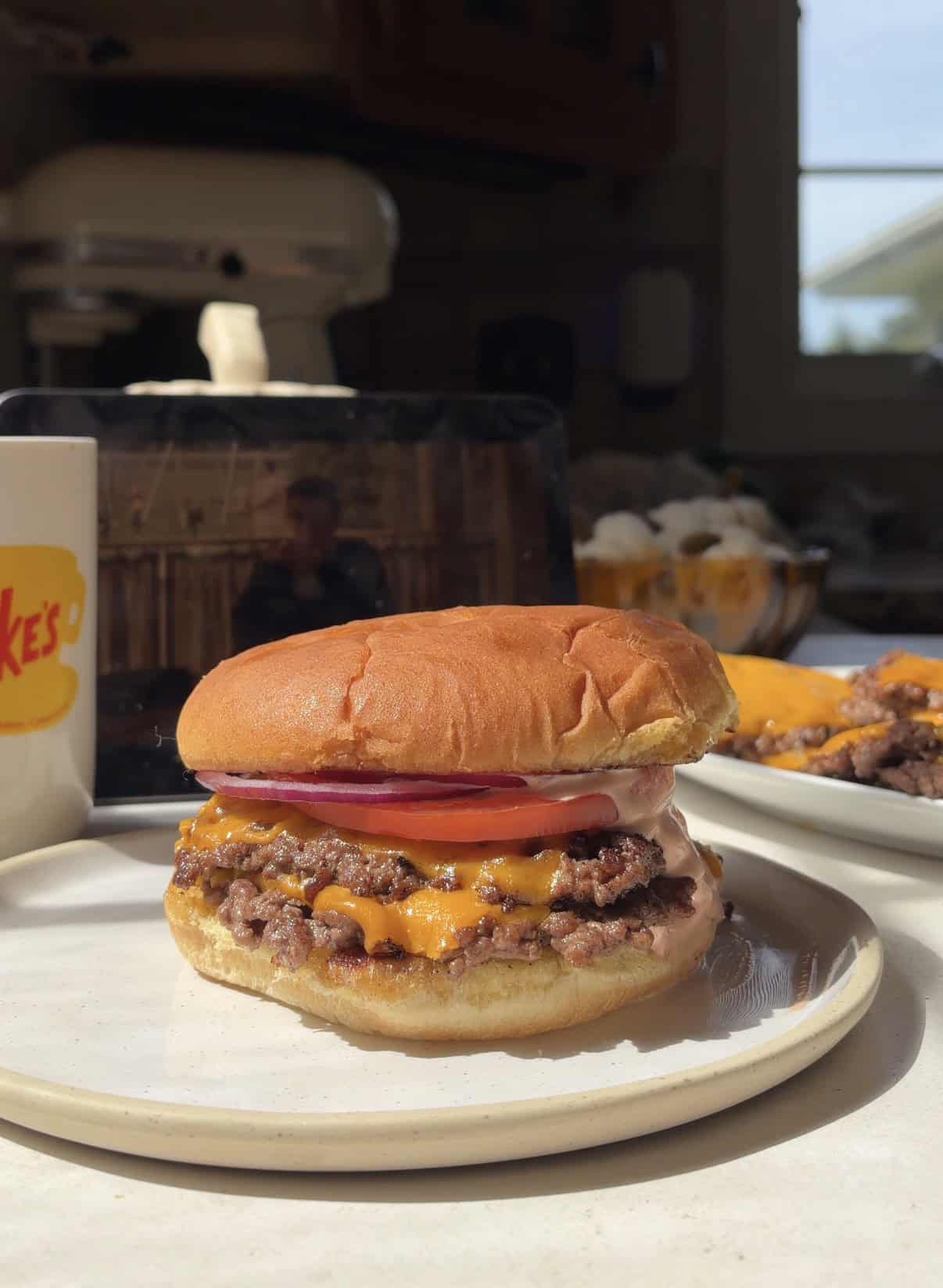 A double cheeseburger with tomato, onion, and sauce on a toasted bun, served on a plate.